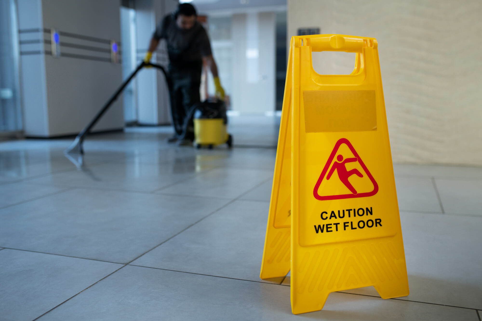 Man cleaning floor in background with wet floor sign in foreground