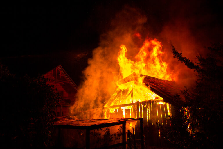 Residential structure engulfed in flames at night, illustrating severe wildfire damage and total property loss.